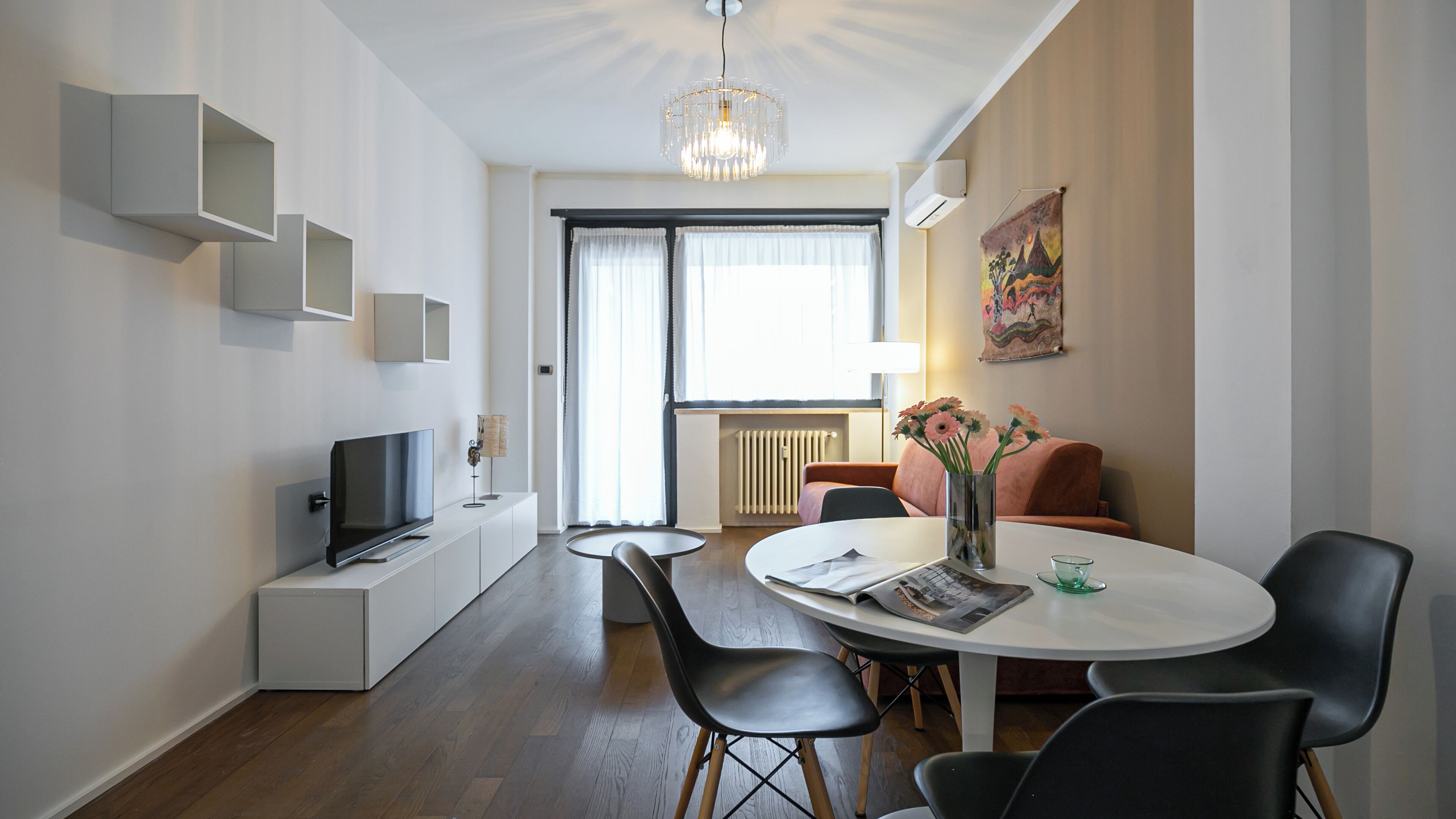Una sala de estar moderna con un televisor de pantalla plana, una mesa de comedor con sillas, un sofá y un jarrón decorativo con flores.