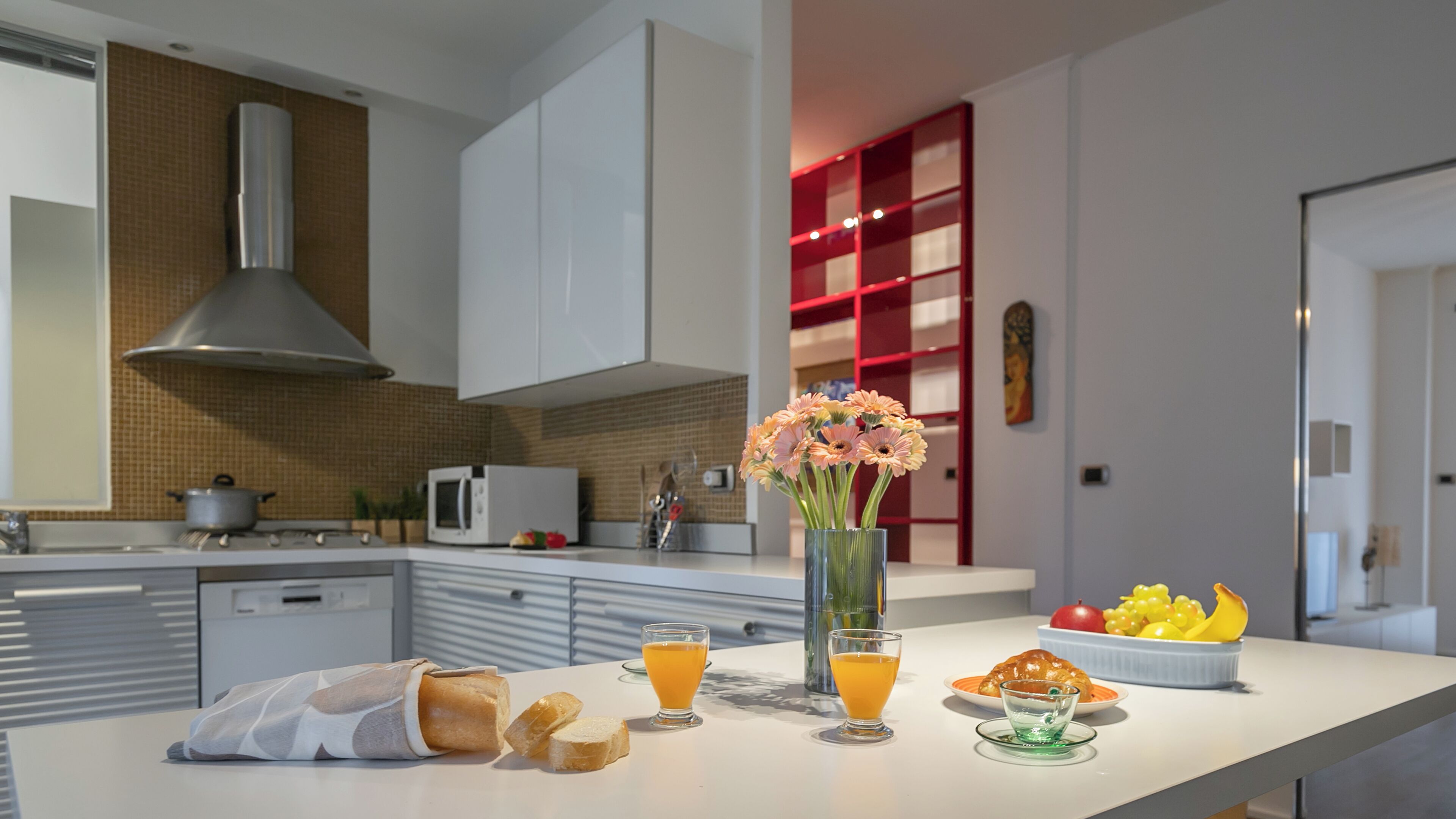 A modern kitchen with white cabinets, a stainless steel range hood, and a red shelving unit.
