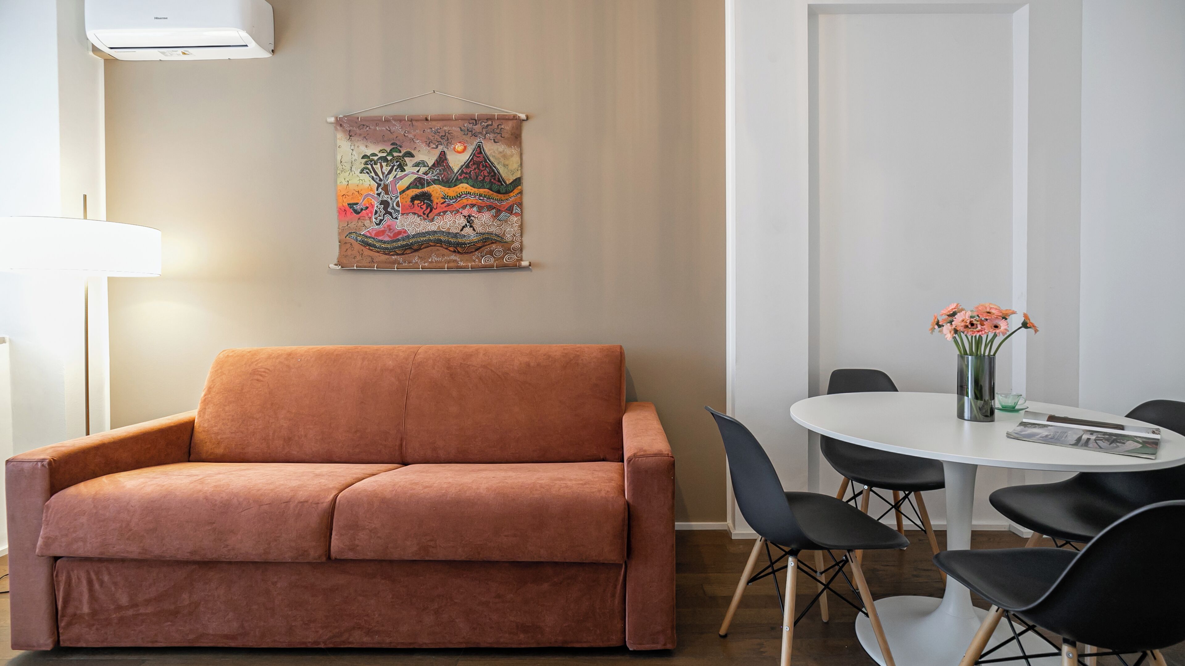 Quarto moderno com sofá marrom, mesa redonda com cadeiras e tapeçaria colorida na parede.