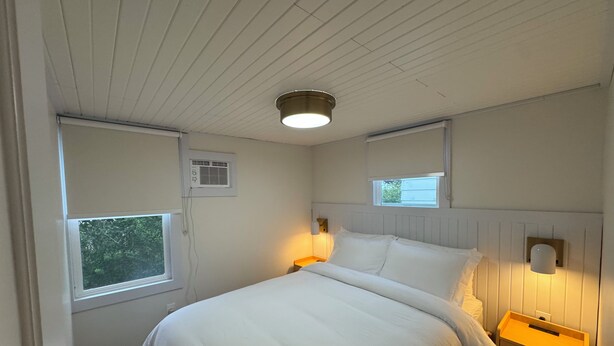 A bedroom with a bed, two bedside lamps, a window, and a wall-mounted air conditioning unit.