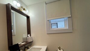 A bathroom with a vanity, a mirror, a sink, a towel, a tissue dispenser, and a window with a view of the outside.