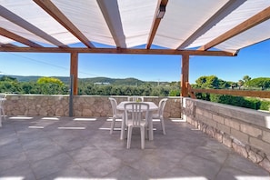 Une terrasse couverte avec un mur en pierre, une table avec des chaises et une vue sur la campagne.