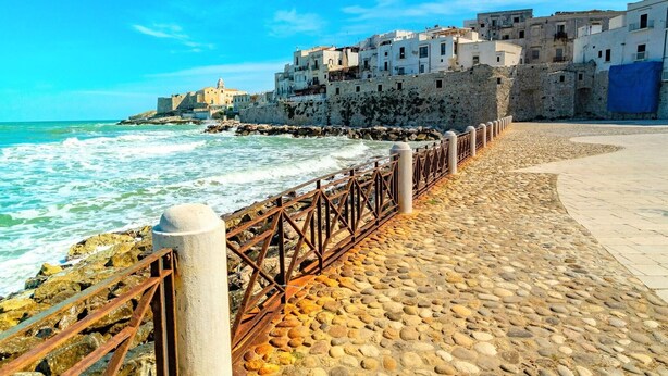 A coastal walkway with a stone-paved path, a metal railing, and buildings in the background. - Apartment 'La Mignola - Bilo 2' with Shared Garden, Wi-Fi and Air Conditioning (Vieste)