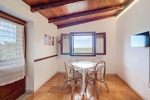 Un coin repas avec un plafond en bois, une table entourée de chaises et une fenêtre agrémentée de rideaux.