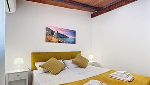 A bedroom with a bed, two bedside tables, a nightstand, a painting of a coastal landscape, and a folded towel on the bed. - Apartment 'La Mignola - Bilo 2 - Duplicate' with Shared Garden, Wi-Fi and Air Conditioning (Vieste)