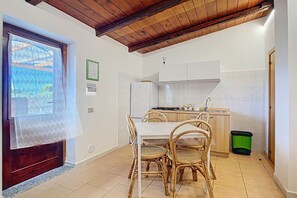 A kitchen with a dining table and chairs, a window with a curtain, and a green trash bin.