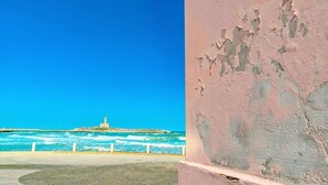 Blick auf die Küste mit einem Leuchtturm, einem gepflasterten Weg und einer verwitterten Mauer.