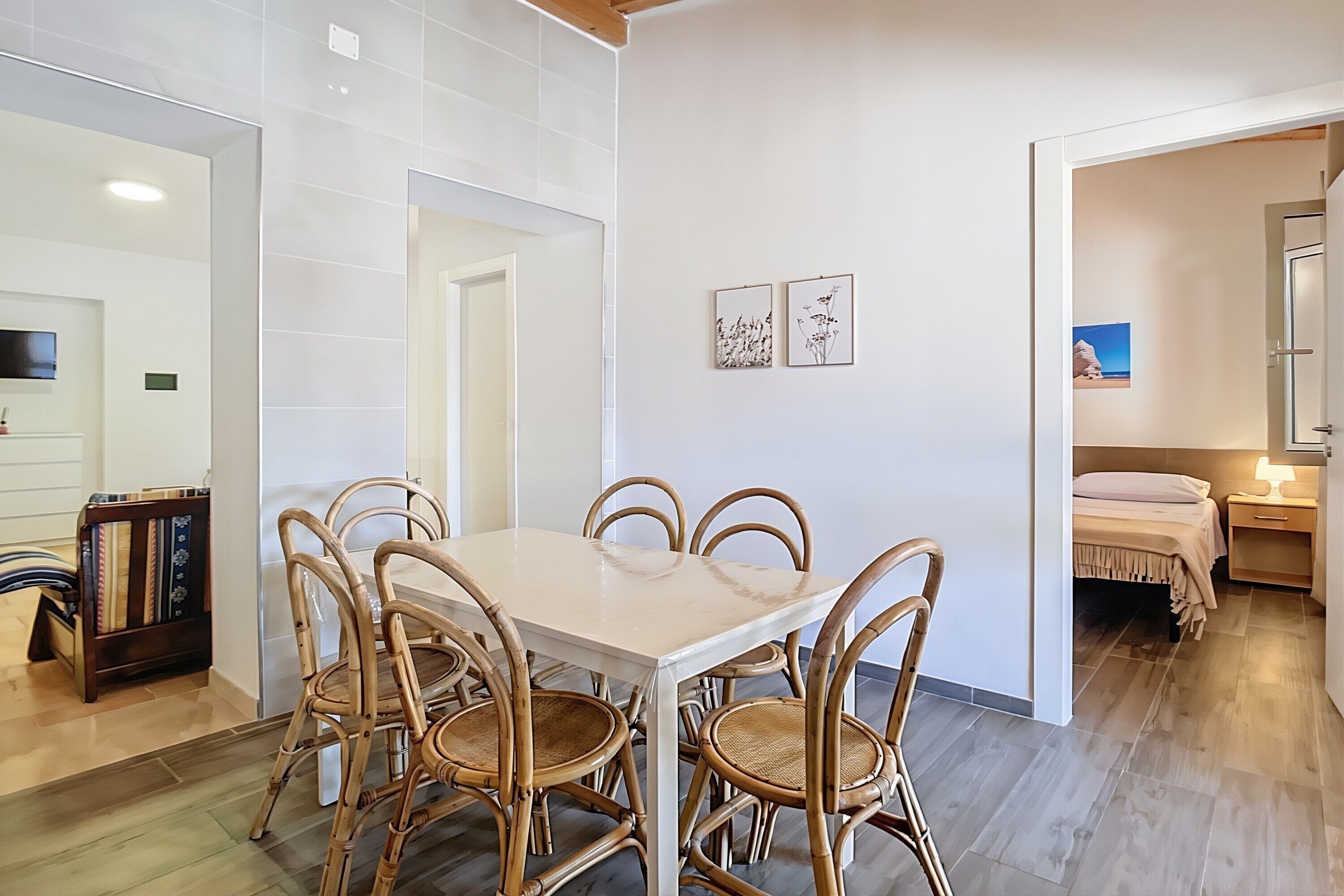 A dining area with a table and chairs, a kitchen area with cabinets, and a bedroom with a bed and nightstand.
