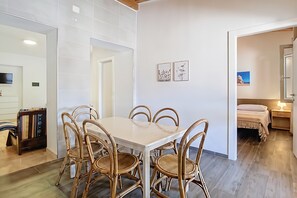 A dining area with a table and chairs, a kitchen area with cabinets, and a bedroom with a bed and nightstand. - Apartment 'La Mignola - Quadri 6' with Private Terrace, Wi-Fi and Air Conditioning (Vieste)