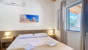 A hotel room with a bed, two bedside lamps, an air conditioner, a framed picture on the wall, and a window with curtains. - Apartment 'La Mignola - Quadri 6' with Private Terrace, Wi-Fi and Air Conditioning (Vieste)