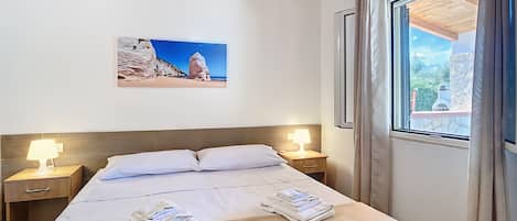 Habitación de hotel con cama, dos lámparas de noche, aire acondicionado, un cuadro en la pared y ventana con cortinas.