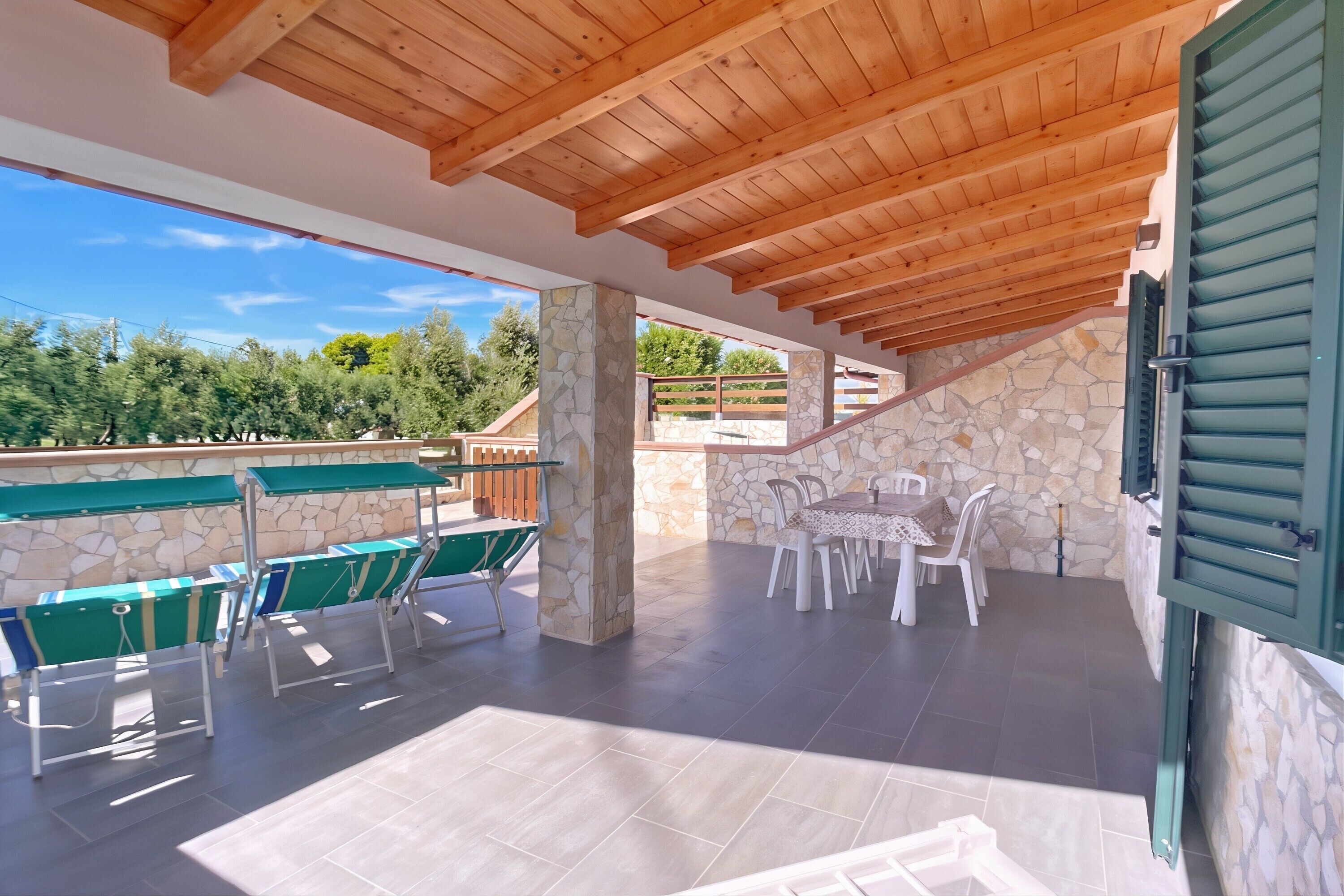 An outdoor patio with stone pillars, wooden ceiling beams, and a stone wall.