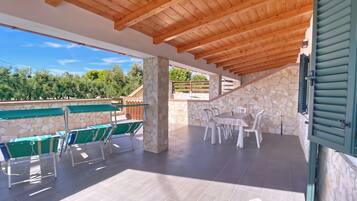 An outdoor patio with stone pillars, wooden ceiling beams, and a stone wall.