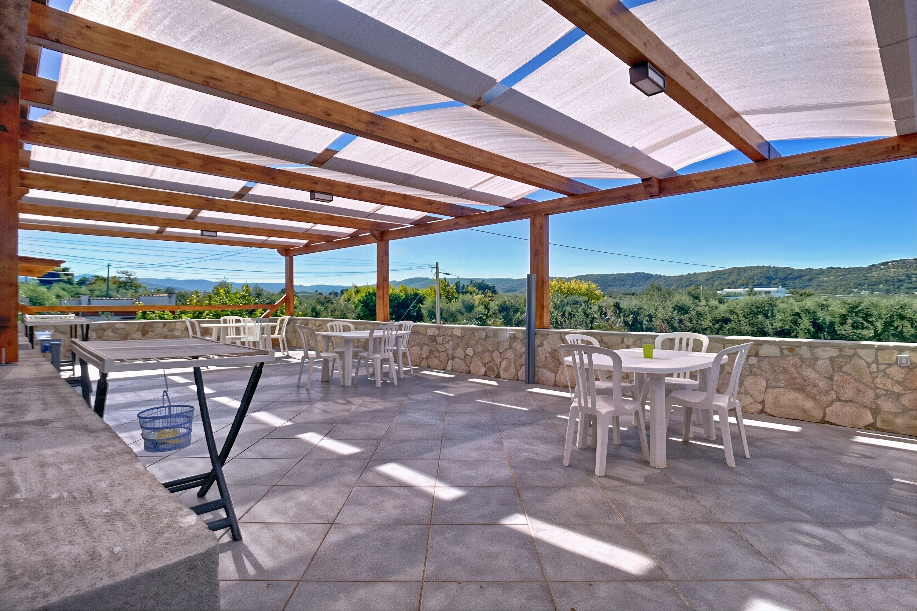Un patio al aire libre con mesas y sillas, un muro de piedra y vistas del paisaje.