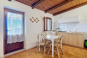 Un coin repas avec une table blanche et des chaises en osier, une cuisine avec des meubles en bois clair et un plafond en bois.