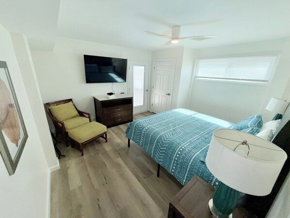 A bedroom with a bed, a chair, a television, a desk, a lamp, and a ceiling fan.