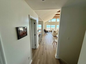 A hallway leading to a living area with a view of the outdoors, a door, and a framed picture on the wall.