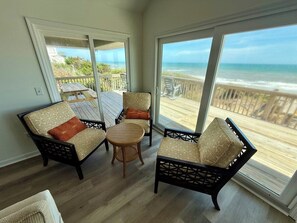 A room with a view of the beach, featuring two chairs, a small table, and a wooden floor. - Salty Haven - Endless Views - Beachfront & Pool - 7BR (Indian Beach)