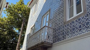 Un edificio con pareti esterne a motivi blu e bianchi, un balcone con ringhiere bianche ornate e un cielo azzurro limpido sullo sfondo.