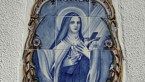 Un'opera d'arte in maioliche blu e bianche raffigura una figura religiosa, incorniciata da decorazioni dorate e rosa elaborate.