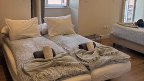 Un letto matrimoniale con coperta e cuscini decorati, un comodino, una TV montata a parete e una finestra con tende.