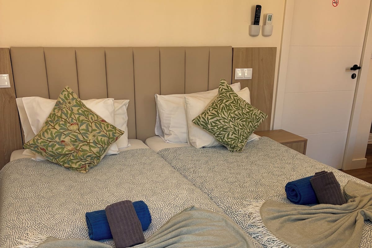 A neatly made bed with patterned bedding and pillows, a bedside table with a remote control, and a door with a no-smoking sign.