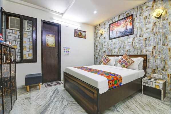 A bedroom with a bed, a nightstand, a dresser, a door, and a wall with a patterned design. - Hotel Midtown (New Delhi)