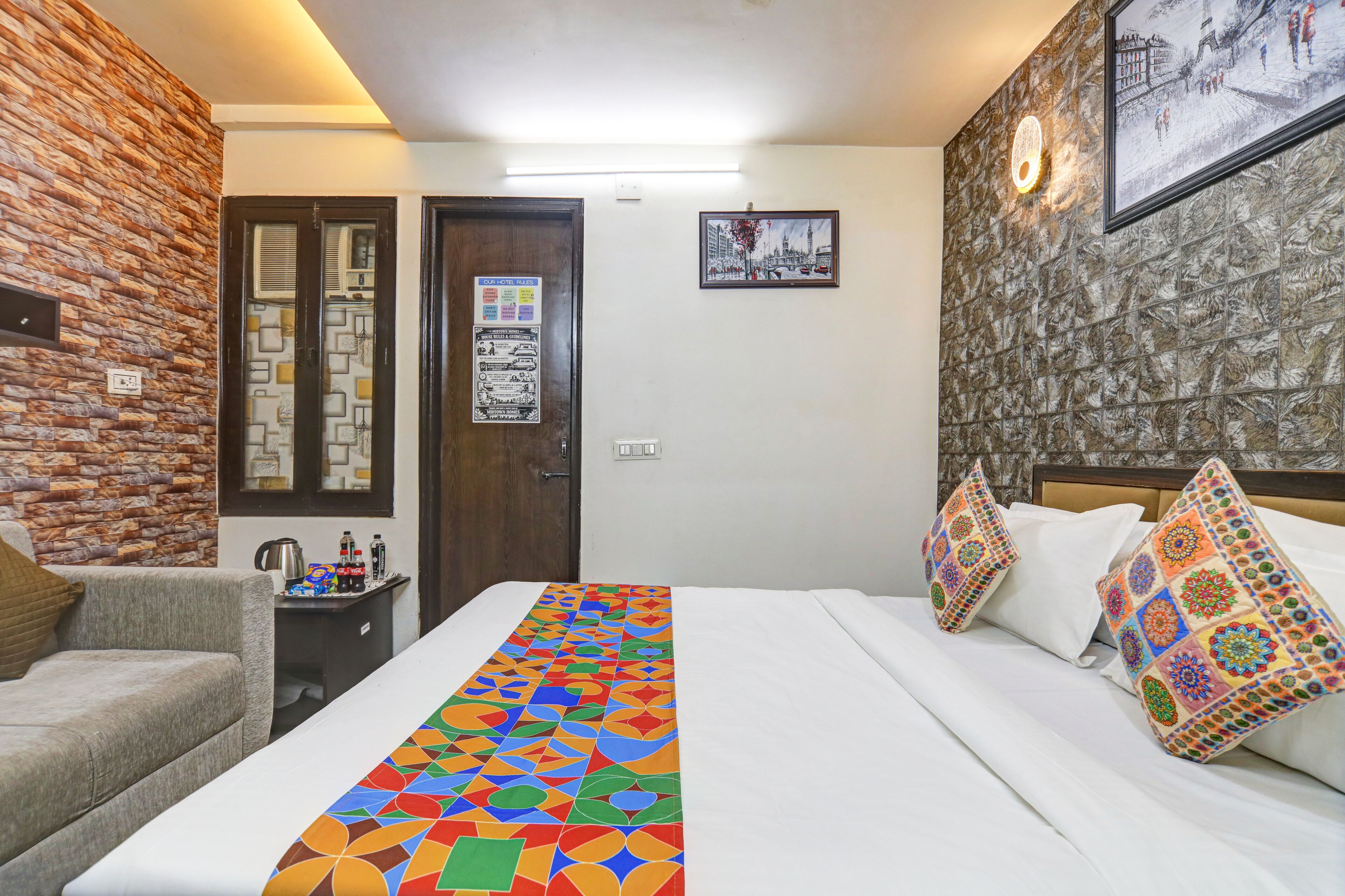 A hotel room with a bed, a sofa, a nightstand, a wall with a patterned design, and a door with a poster.