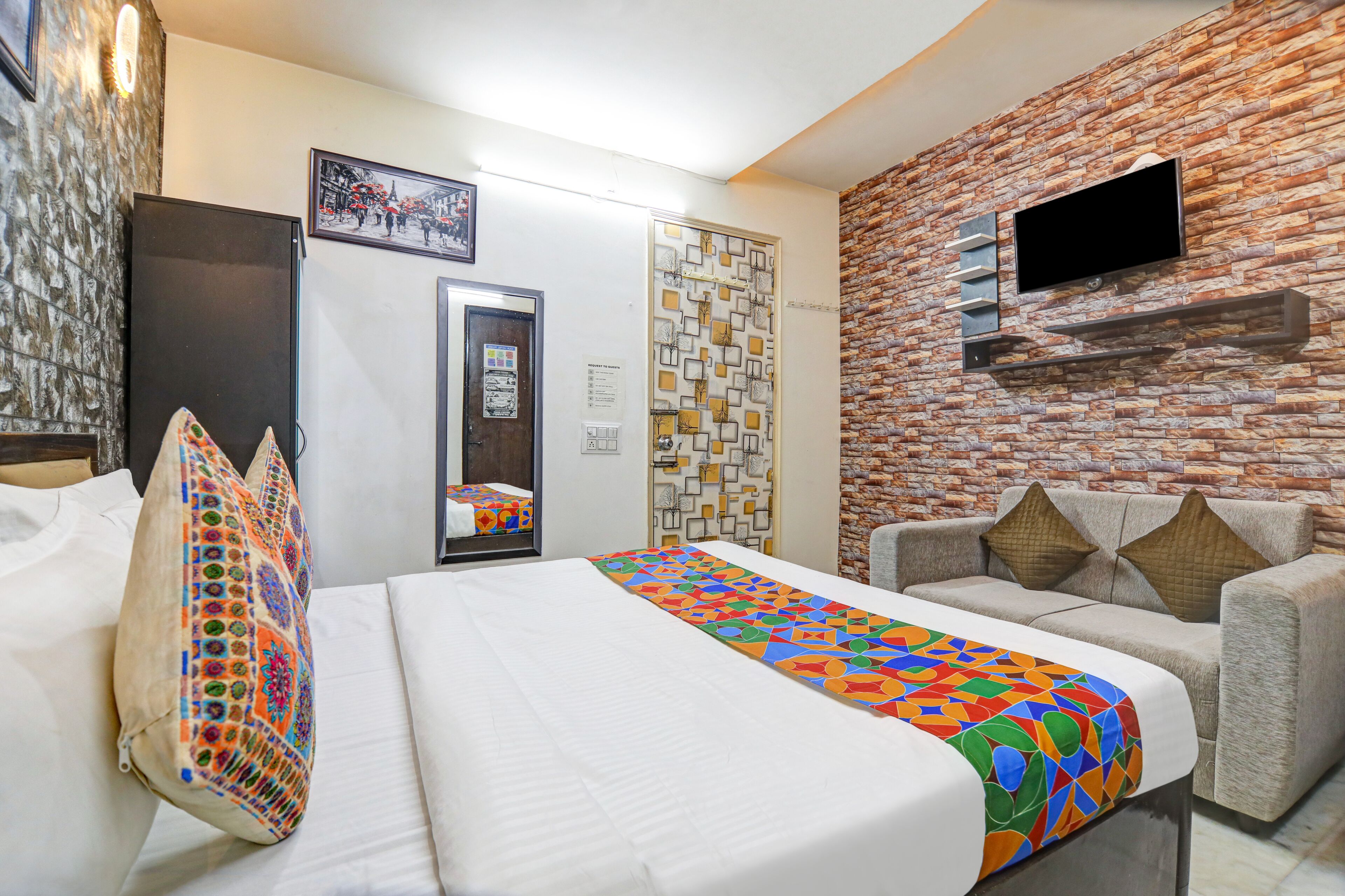 Quarto de hotel com cama, sofá, televisão fixada numa parede de pedra e um detalhe decorativo na parede com padrão.