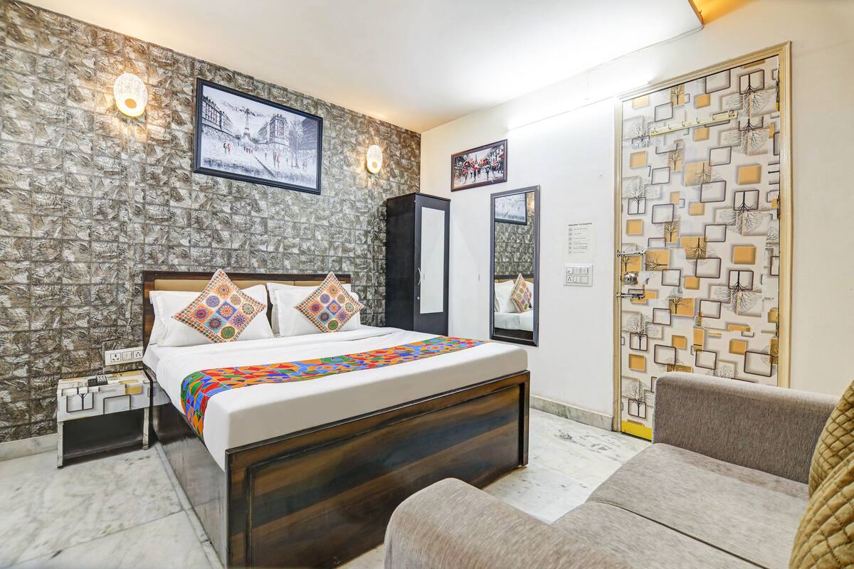 Un dormitorio con pared de piedra simulada, una cama con almohadones coloridos, una mesita de noche, un armario y una puerta con diseño geométrico.