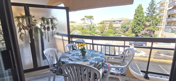 A balcony with a table and chairs, a hanging plant, and a view of buildings and trees.