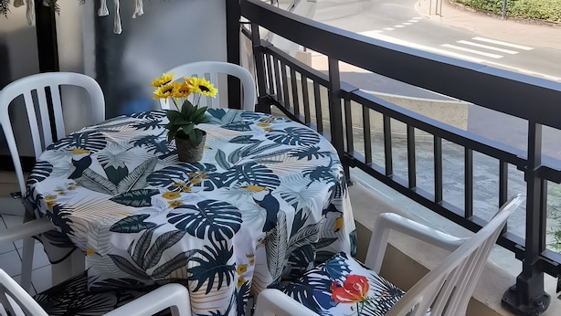 A balcony with a table and chairs, a view of a building, and hanging plants.