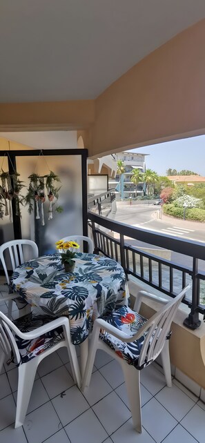 A balcony with a table and chairs, a view of a building, and hanging plants.