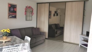 A living room with a sofa, a dining table with a sunflower centerpiece, a sliding door to a bedroom, and a TV on a stand.