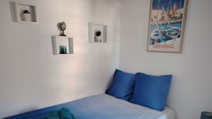 A bedroom with a bed, pillows, a rolled towel, and a framed picture on the wall.