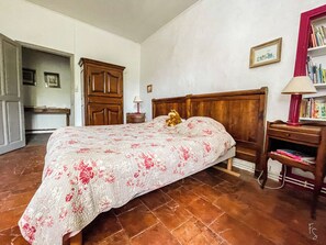 A bedroom with a wooden bed, a nightstand with a lamp, a bookshelf, and a door leading to another room.