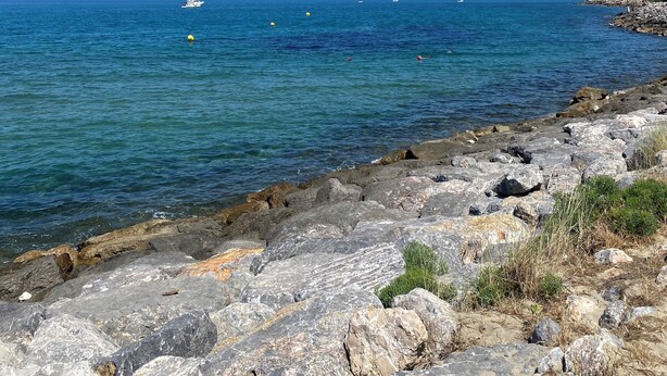 Una costa rocciosa con mare cristallino e imbarcazioni all'orizzonte.