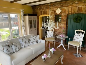 Un salon avec un canapé, deux fauteuils, une table basse, une horloge et un mur en briques.