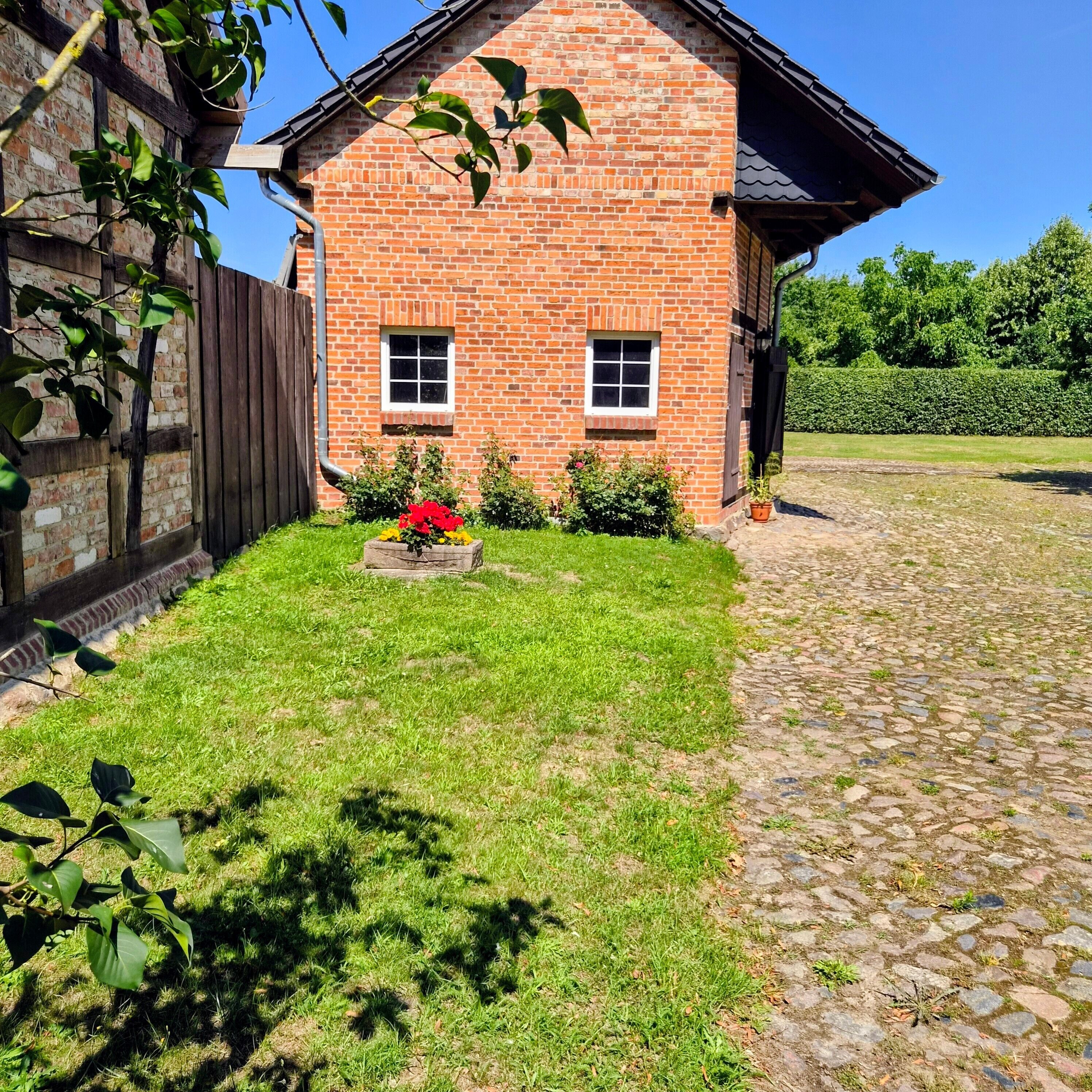 Ein Backsteinhaus mit befestigter Auffahrt und einem kleinen Garten mit Blumen.