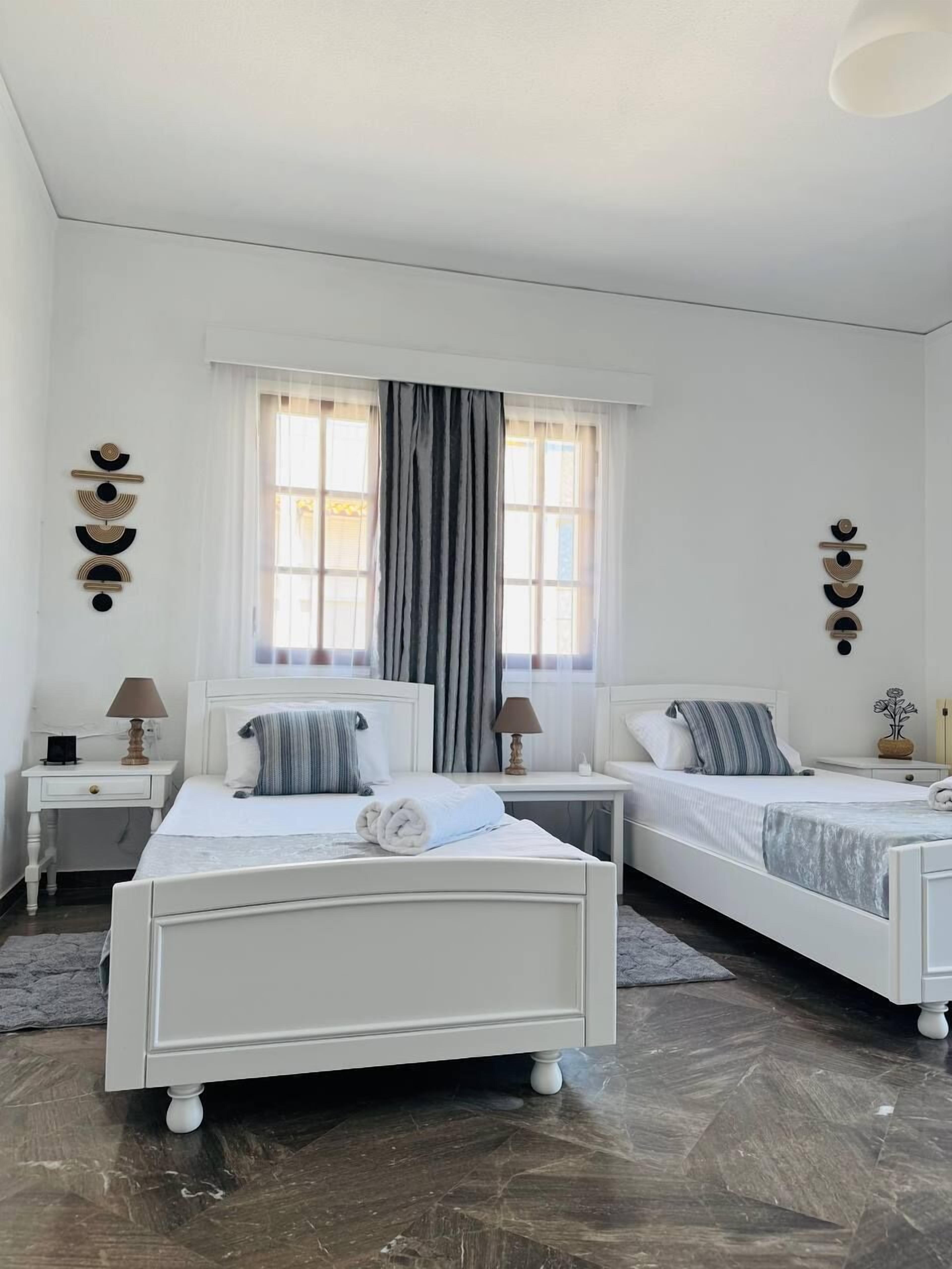 A hotel room with two beds, a large window with curtains, and wall decor.