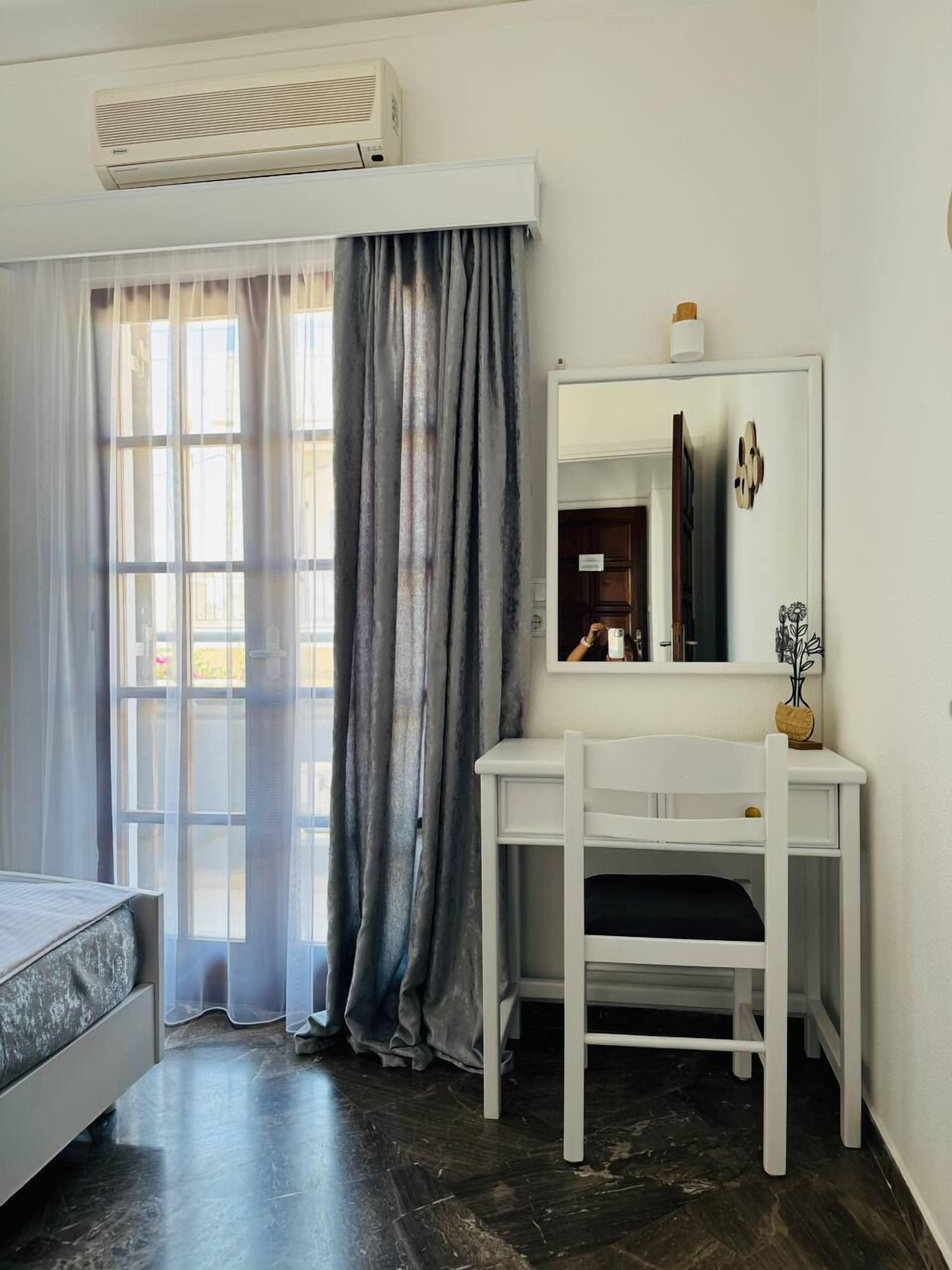 Una habitación con cama, escritorio, espejo y aire acondicionado.