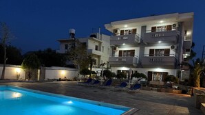 A swimming pool with lounge chairs, a multi-story building with balconies, and outdoor lighting. - Desire Apartments (Kato Gouves)