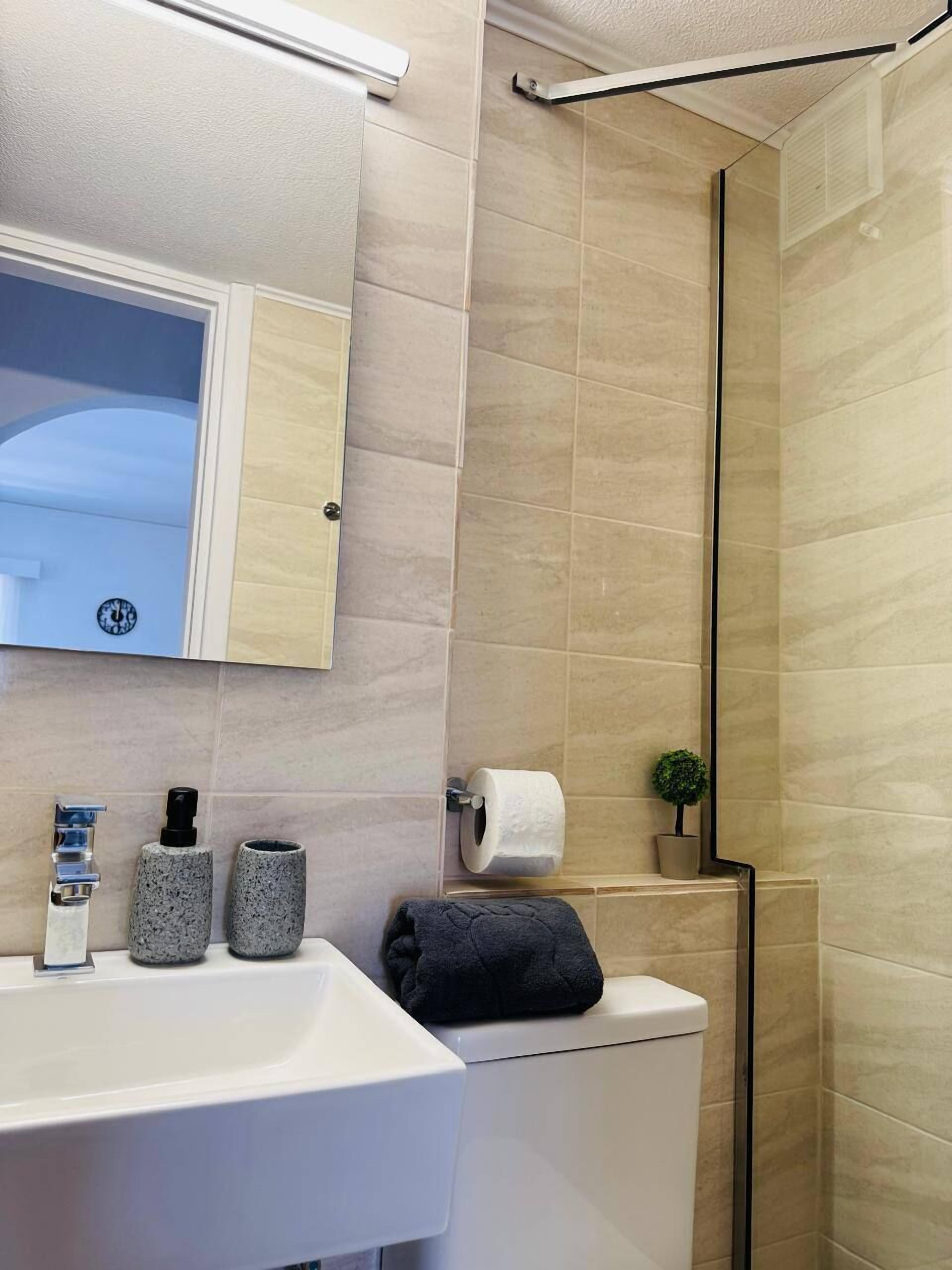 Un baño moderno con lavamanos blanco, espejo, inodoro y zona de ducha.