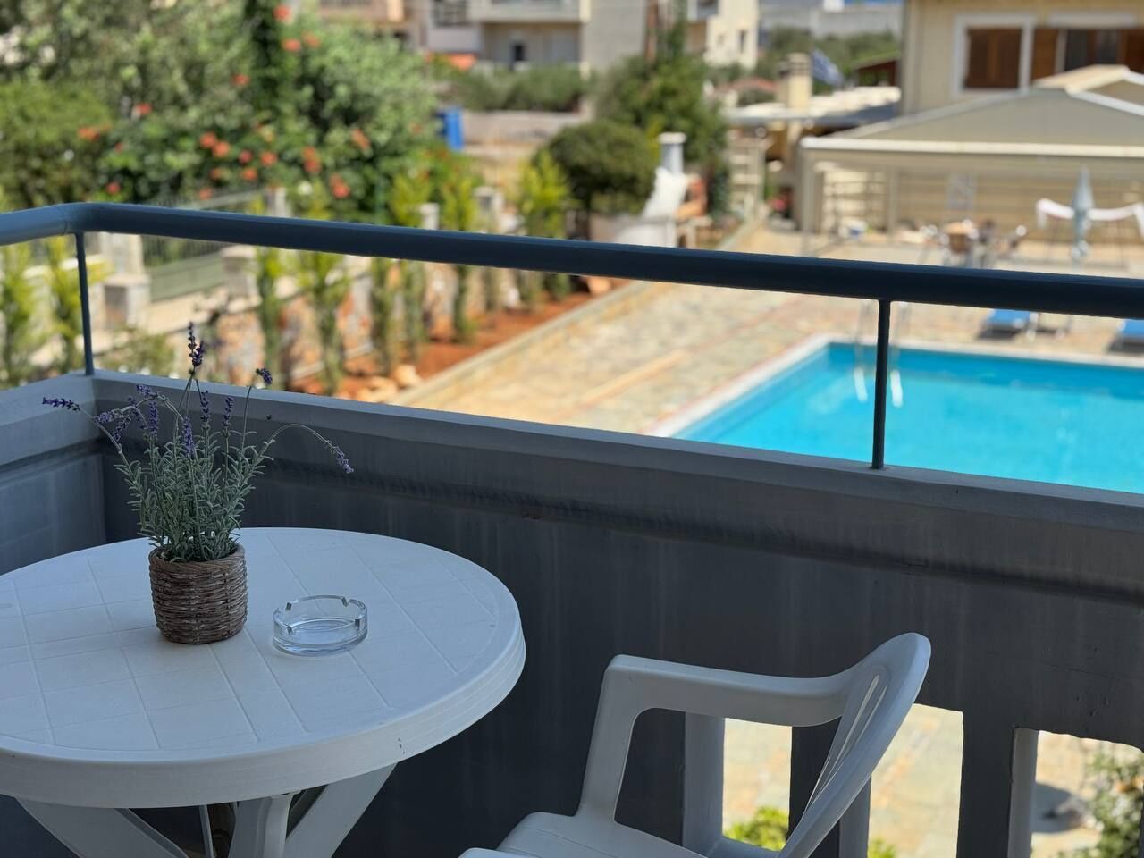 A balcony with a white table and chair, overlooking a swimming pool and a garden.
