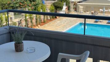 A balcony with a white table and chair, overlooking a swimming pool and a garden.