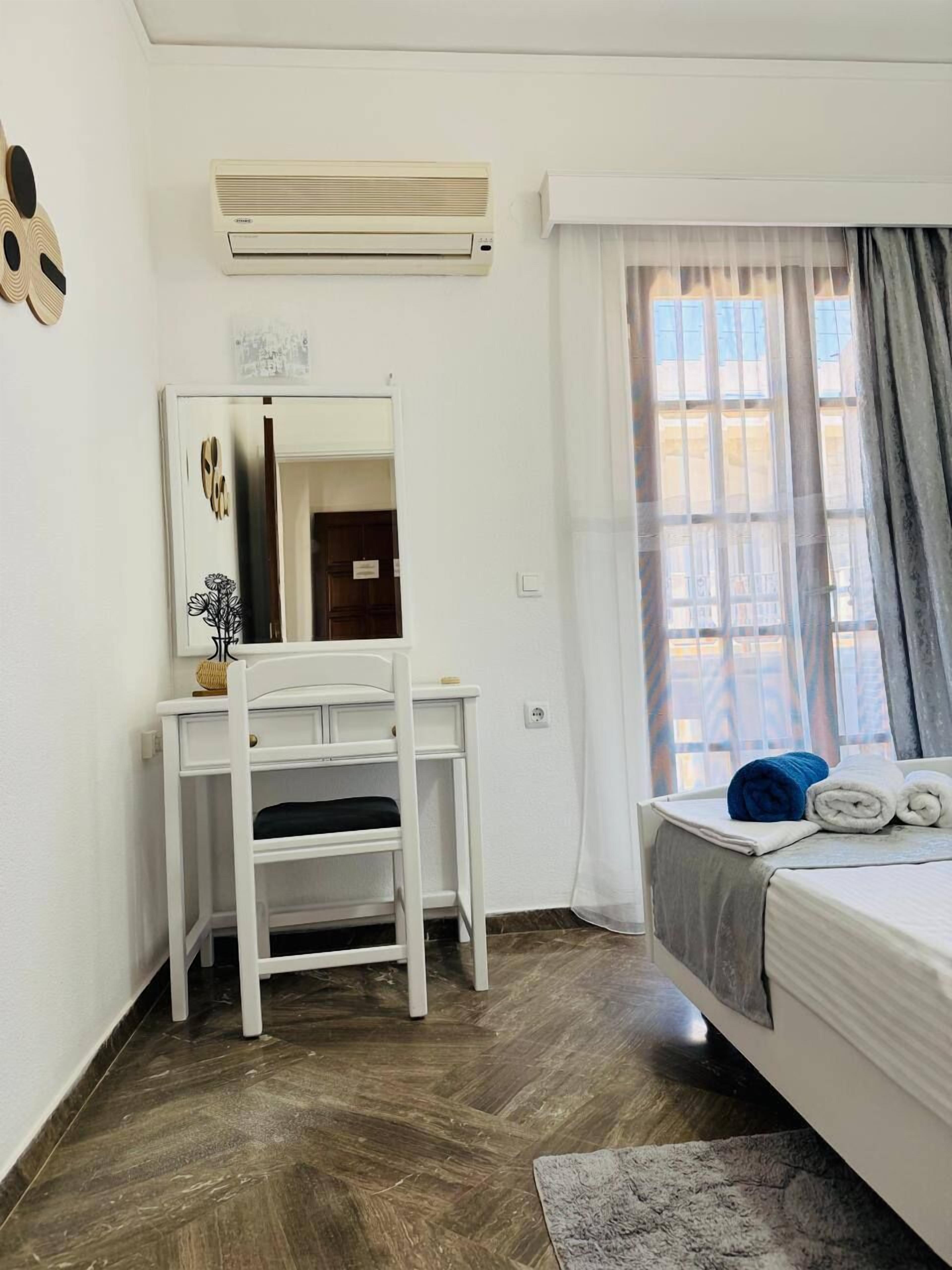 Un dormitorio con cama, escritorio, espejo y ventana con cortinas.