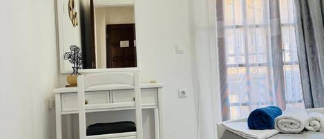 Un dormitorio con cama, escritorio, espejo y ventana con cortinas.