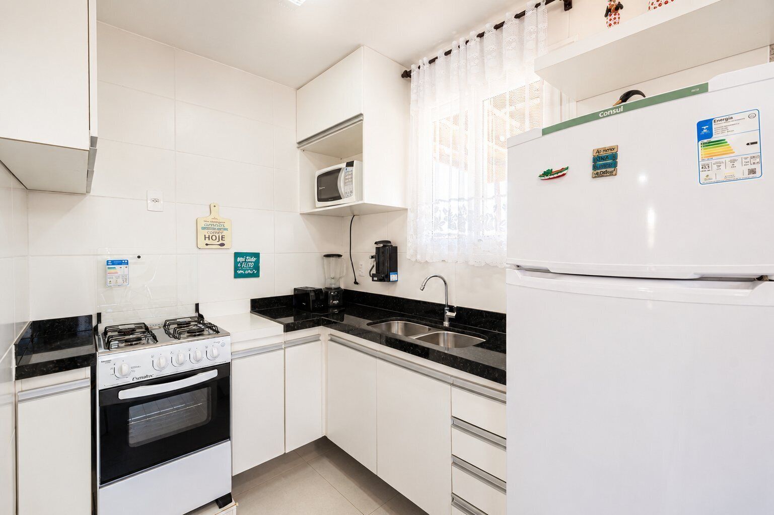 Une cuisine avec des meubles blancs, une cuisinière à gaz, un four à micro-ondes, un évier et un réfrigérateur.