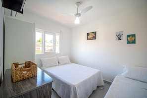 Une chambre à coucher comprenant un lit, un bureau, une chaise, un ventilateur de plafond et deux tableaux accrochés au mur.