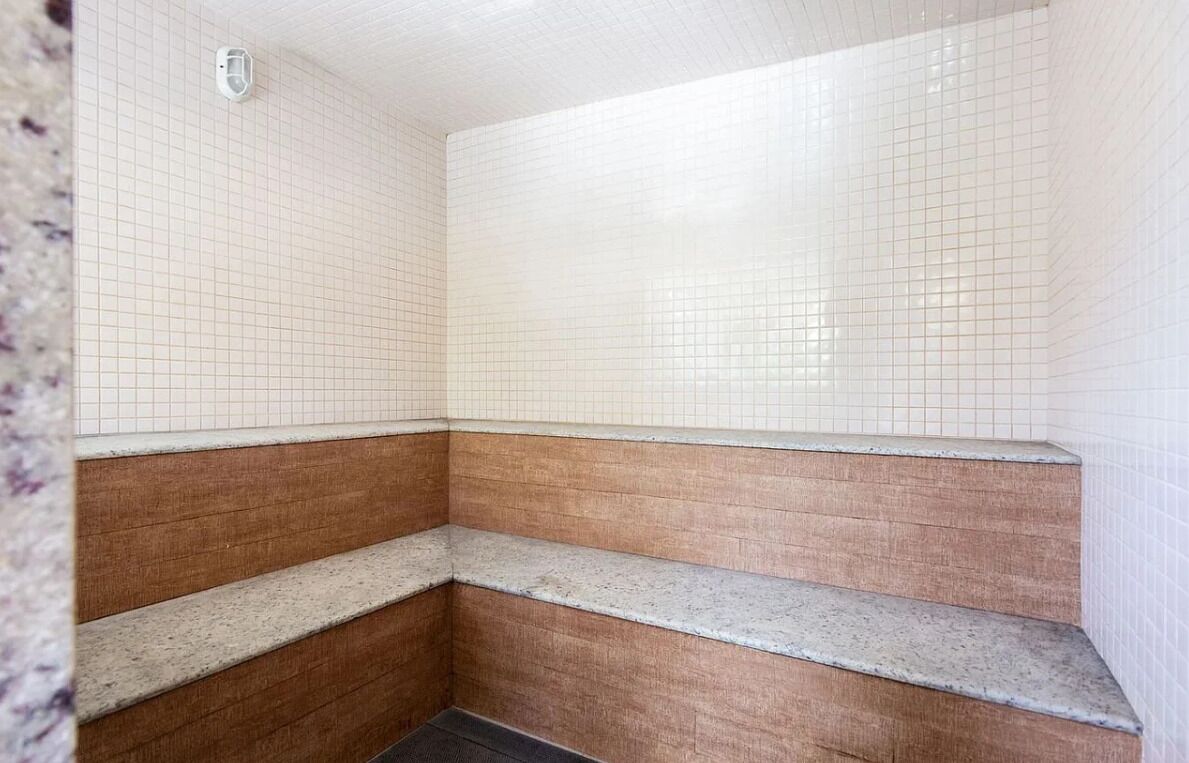 A bathroom with white tiled walls, a wooden bench, and a tiled floor.